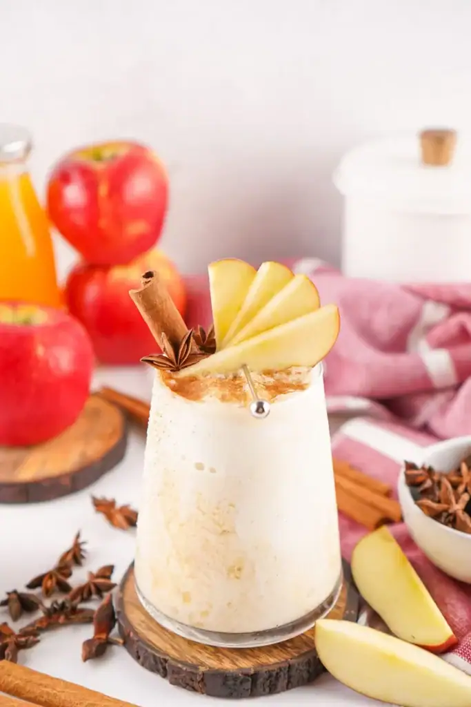 Apple cider float in a glass topped with sliced apple.
