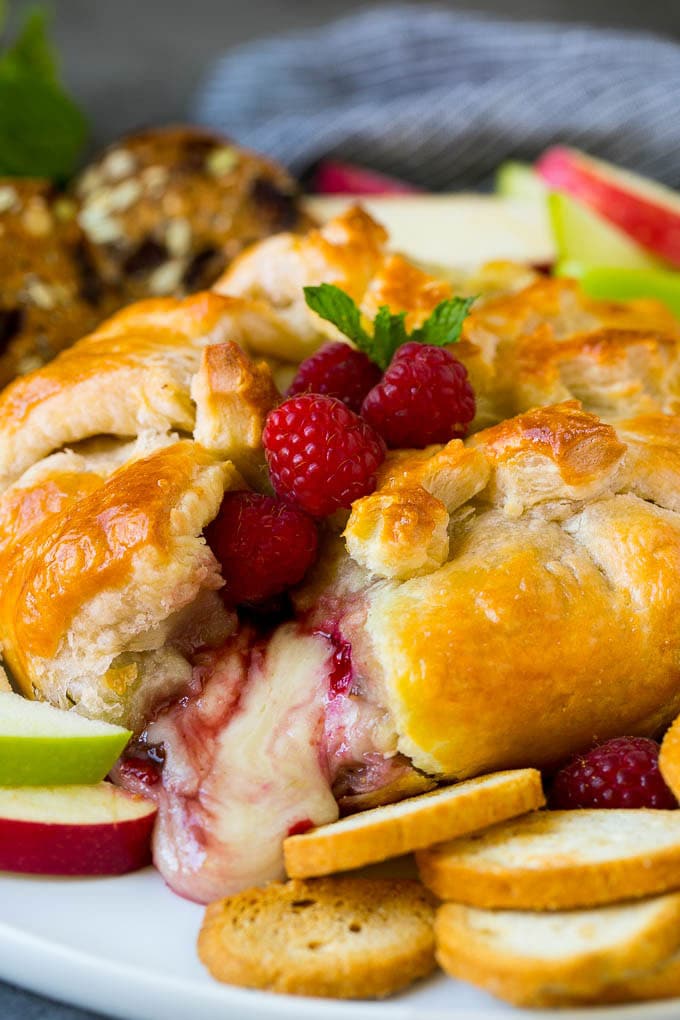 Baked brie with raspberries and crackers on a plate.