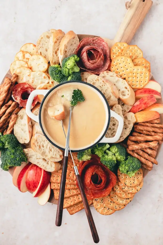 Beer cheese fondue board with bread, crackers, apples, and broccoli.