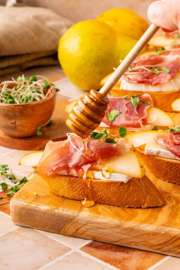 Brie crostini with prosciutto on a wooden board.