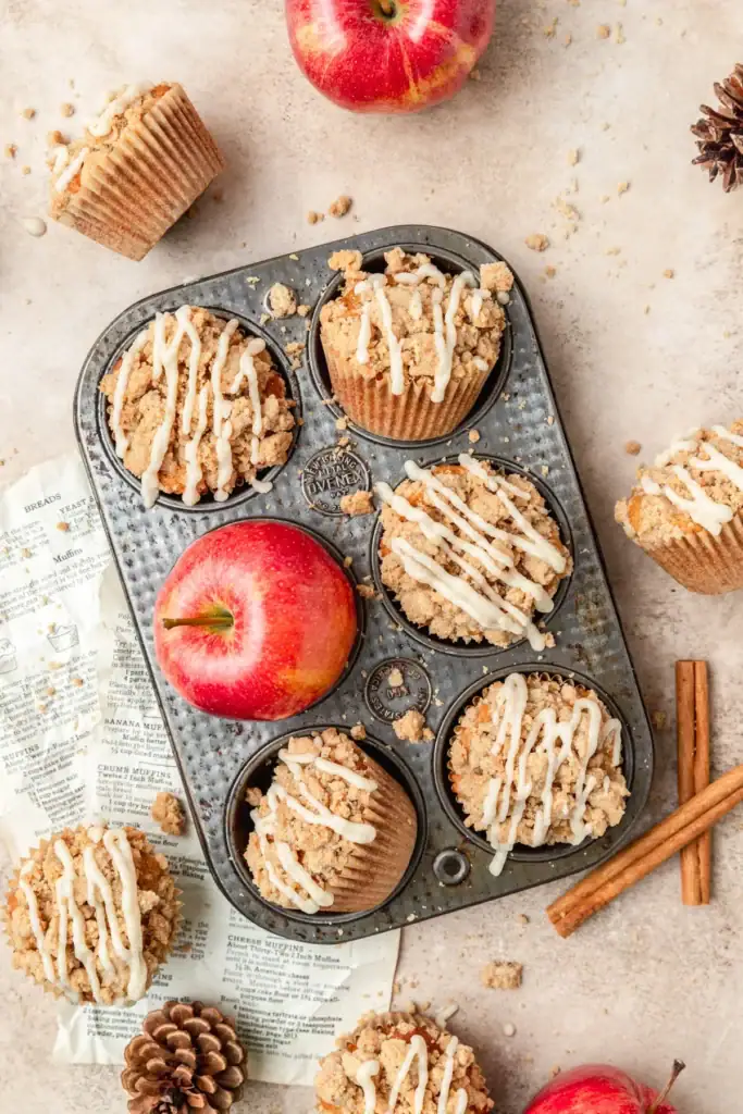 Brown butter apple cider muffins with streusel and glaze on a muffin tray.