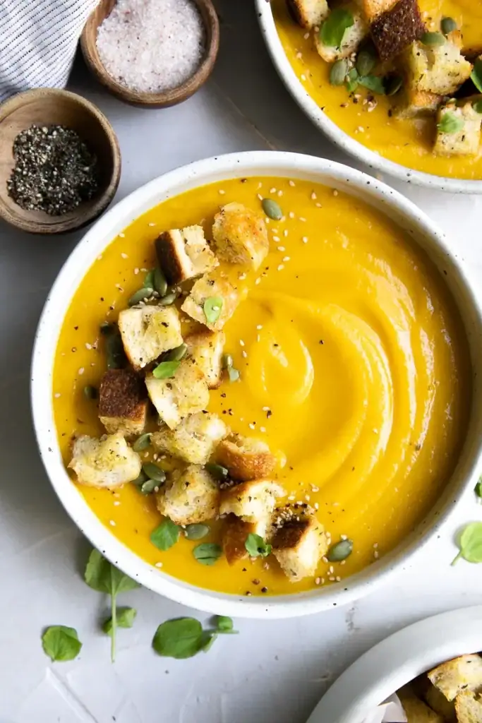 Butternut squash soup with bacon and pomegranates served in a bowl.