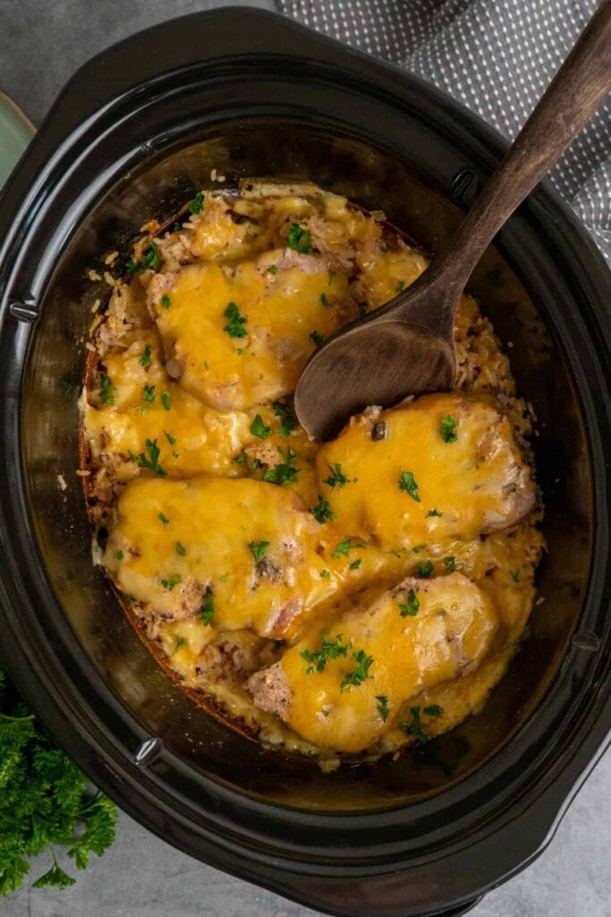 Crock Pot Pork Chops and Rice topped with melted cheese and fresh herbs.