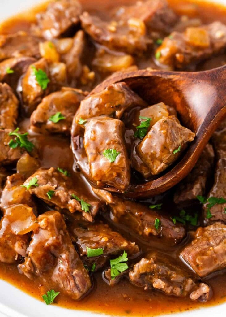 Close-up of crockpot beef tips and gravy on a wooden spoon.