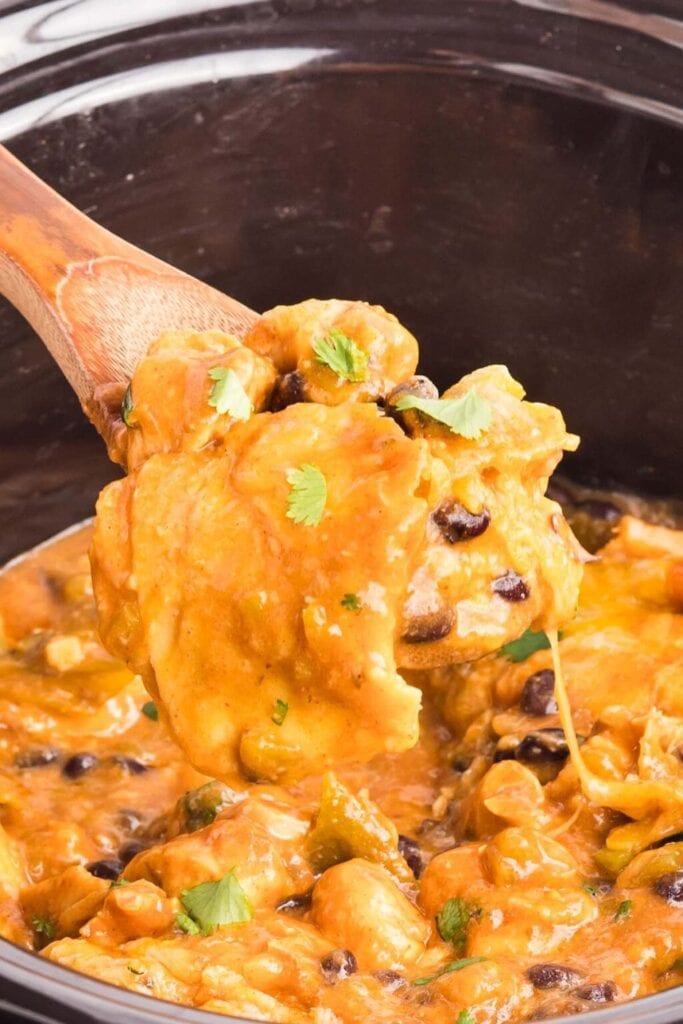 Close up of crockpot chicken enchilada casserole on a wooden spoon.