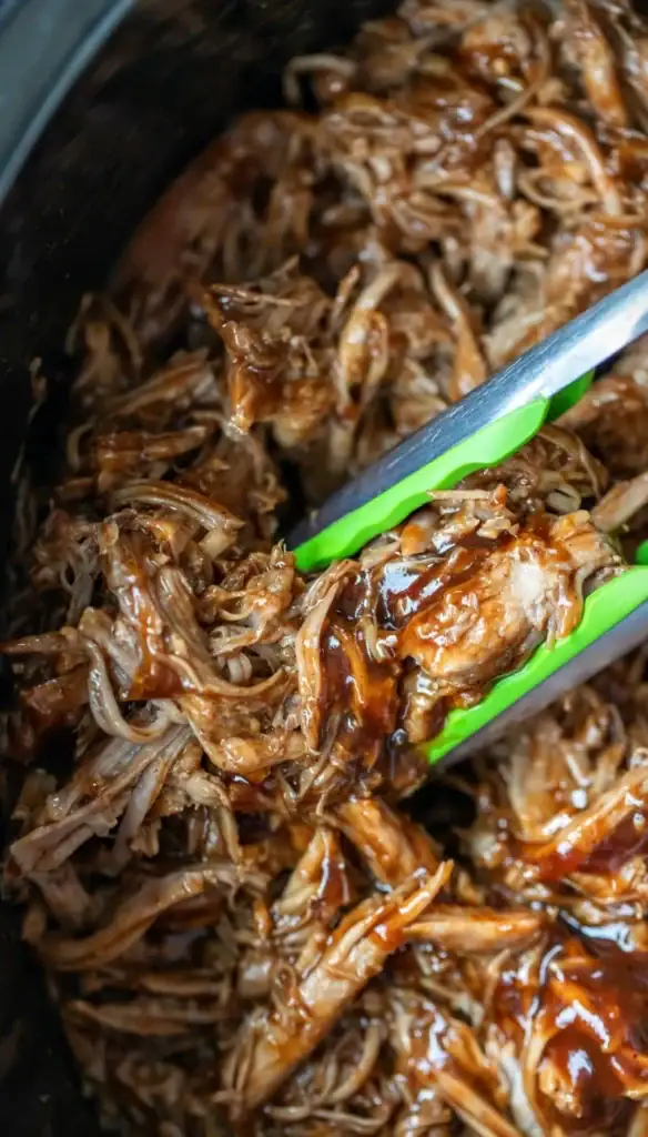 Close-up of crockpot pulled pork with tongs.