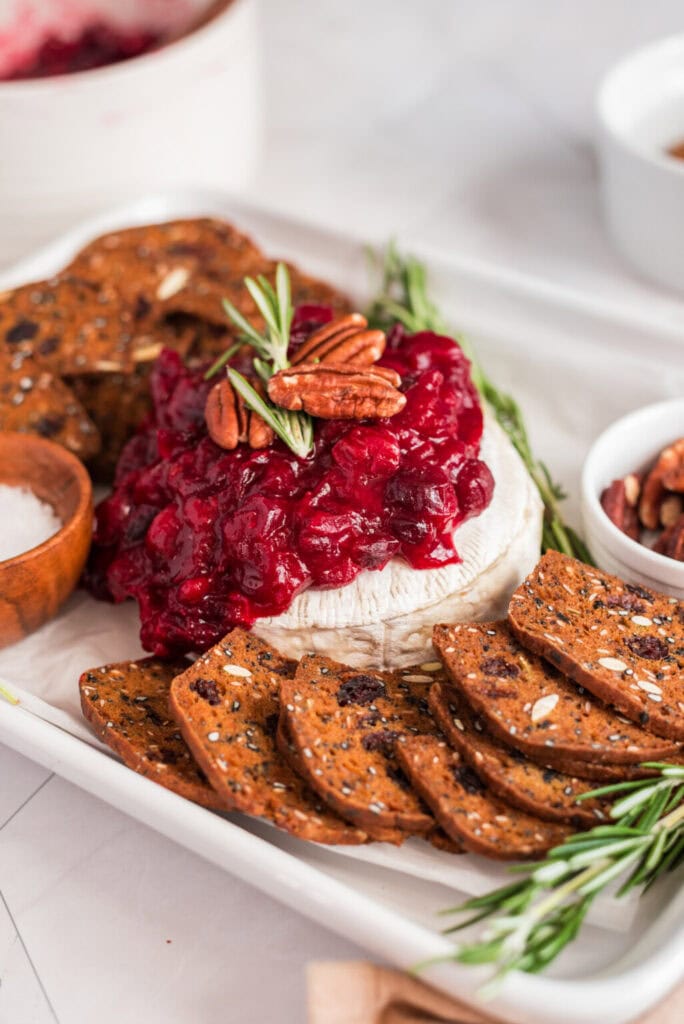 Holiday cranberry baked brie with pecans and crackers on a serving tray.