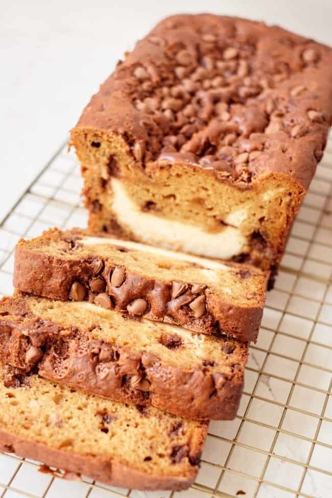 Pumpkin bread with cream cheese filling and chocolate chips on a cooling rack.