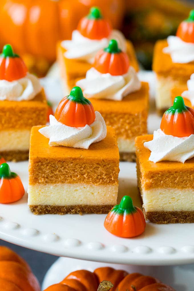 Pumpkin cheesecake bars topped with whipped cream and pumpkin candies.