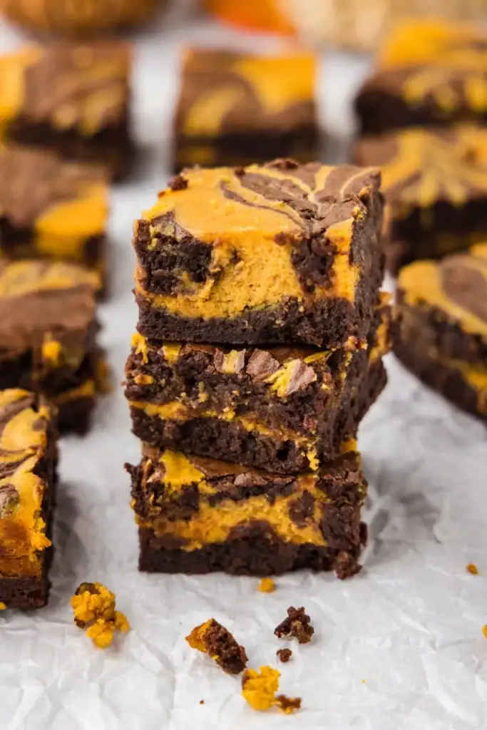 Stack of pumpkin cheesecake brownies on parchment paper.