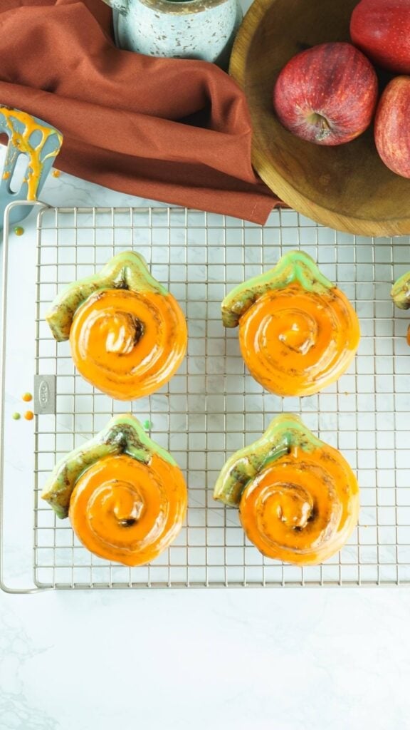 Pumpkin shaped cinnamon rolls on a cooling rack.