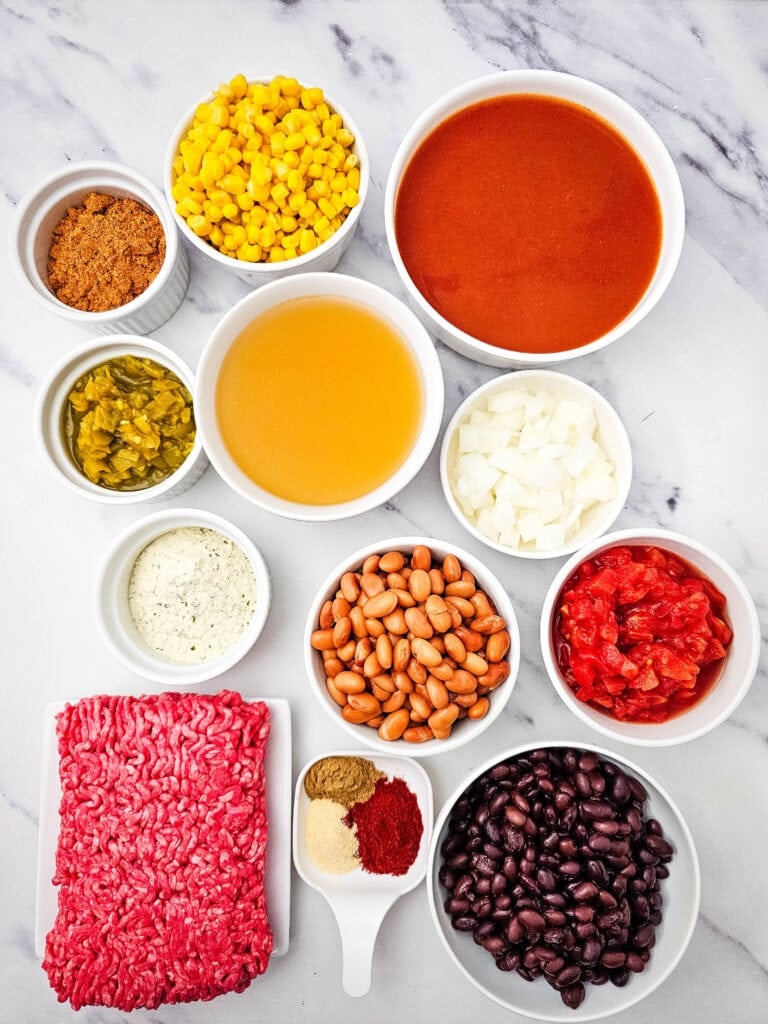 Ingredients for 7 Can Taco Soup with Ground Beef arranged in bowls on a marble surface.
