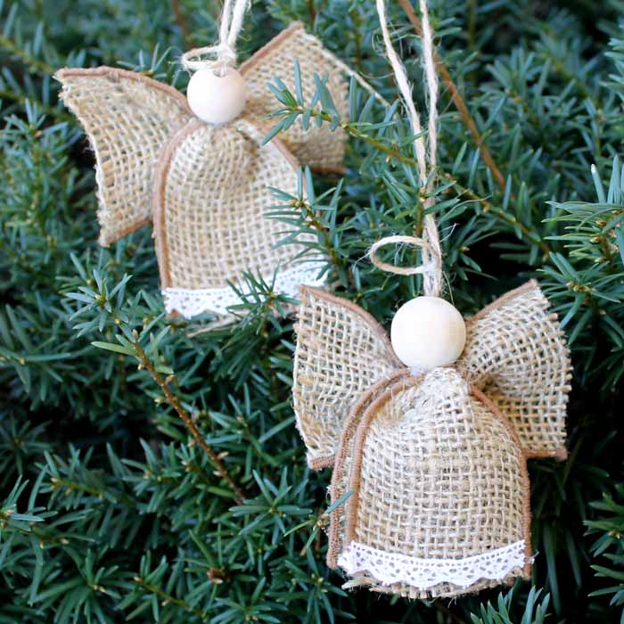 Two burlap angel ornaments with wooden bead heads, lace trim, and twine loops, hanging on evergreen tree.