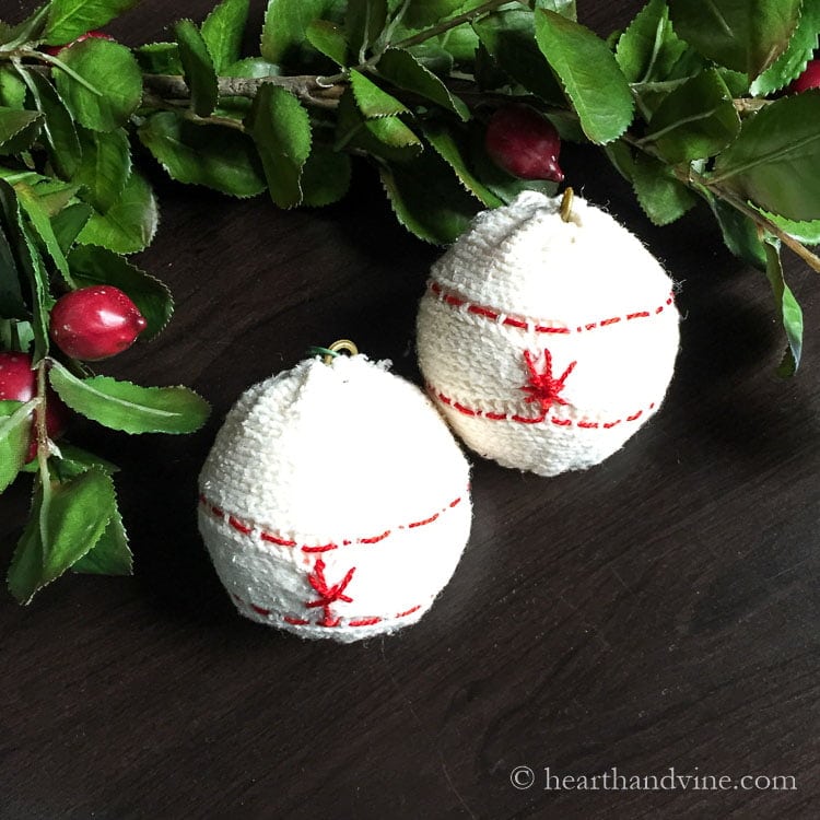 Two handmade ball ornaments wrapped in white cable-knit sweater fabric with red embroidery stitching