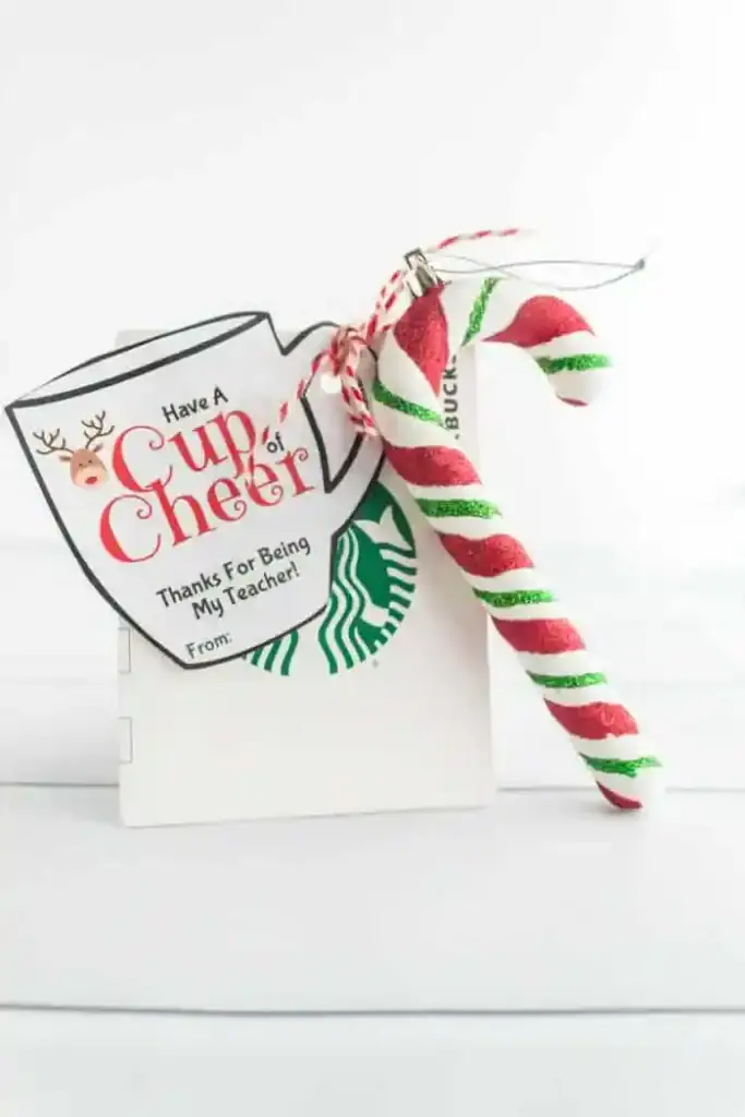Festive gift with Starbucks card, striped candy cane, and coffee cup tag featuring reindeer illustration and text “Have A Cup of Cheer Thanks For Being My Teacher!” tied with red and white twine.