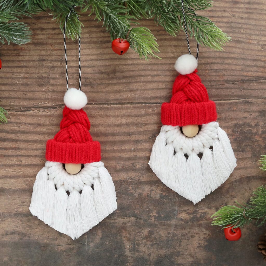 Two handmade macrame Santa ornaments with red yarn hats, white cord beards, and wooden bead noses