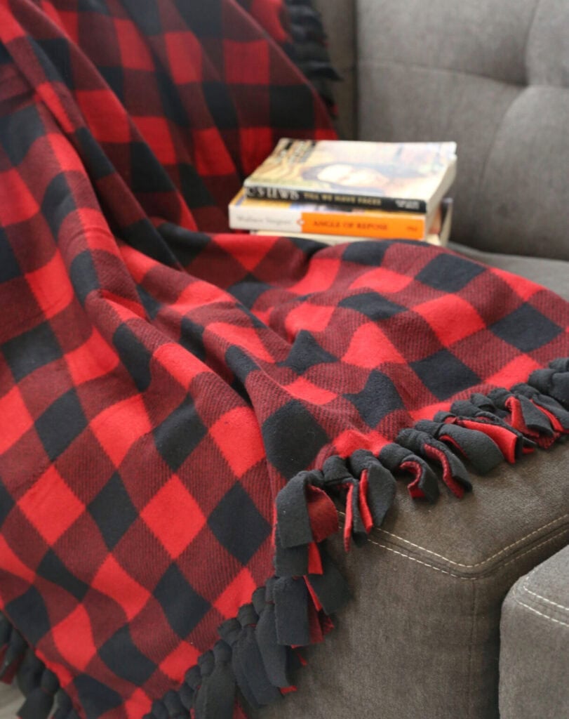Red and black checkered fleece blanket draped on gray couch arm, with two paperback books stacked on seat.