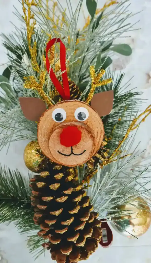 Handmade Rudolph ornament made from wood slices with a red pom-pom nose, googly eyes, and pipe cleaner antlers.