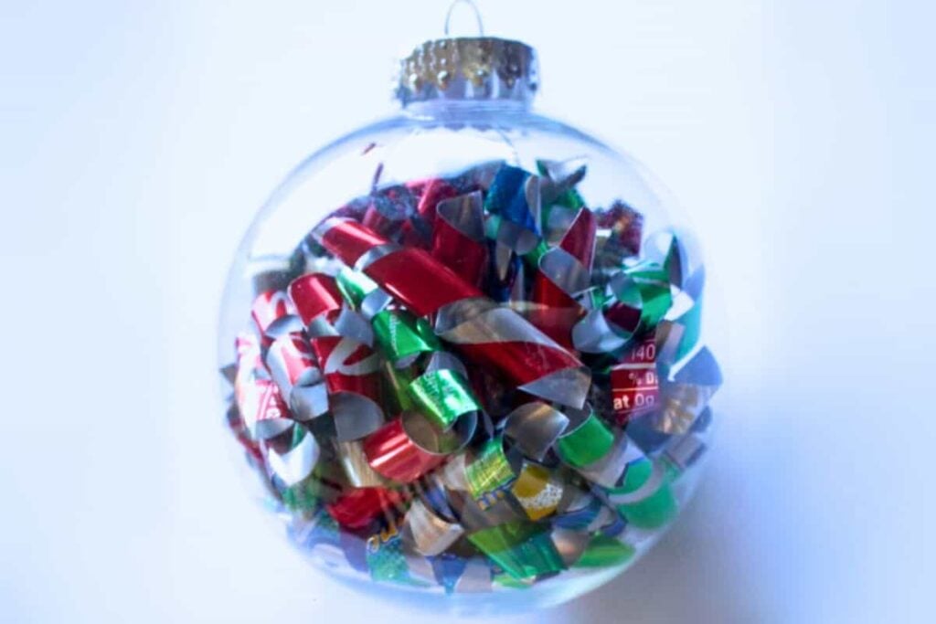 Clear ornament filled with curled metallic strips in red, green, silver, and gold, capped with silver top and hanging loop.