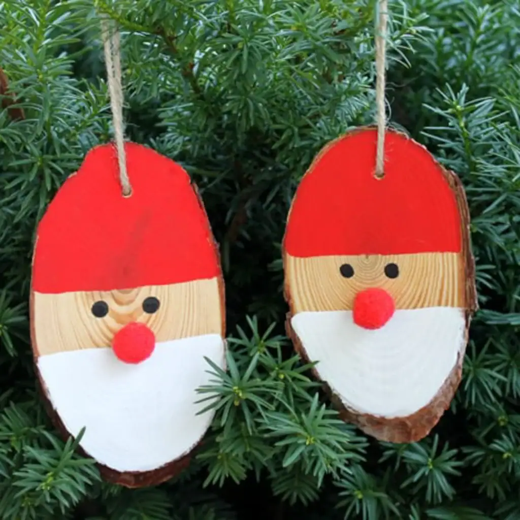 Wood slice ornaments painted as Santa faces with red hats, white beards, pom-pom noses, and twine loops, hanging against pine foliage.