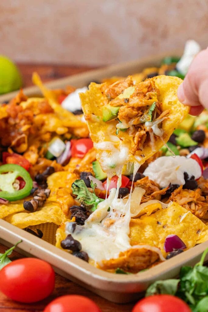 Chicken nachos with melted cheese and toppings on a baking sheet.