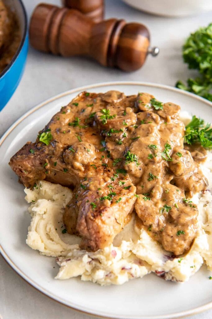Cream of mushroom pork chops over mashed potatoes on a plate.