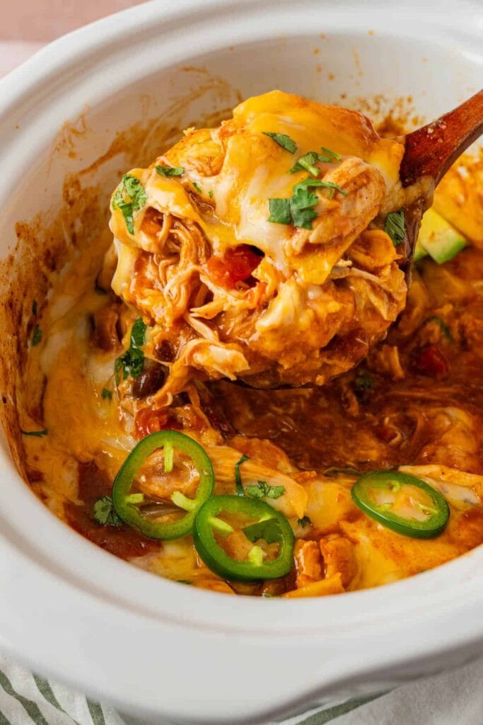 Close-up of crockpot chicken enchiladas on a wooden spoon.