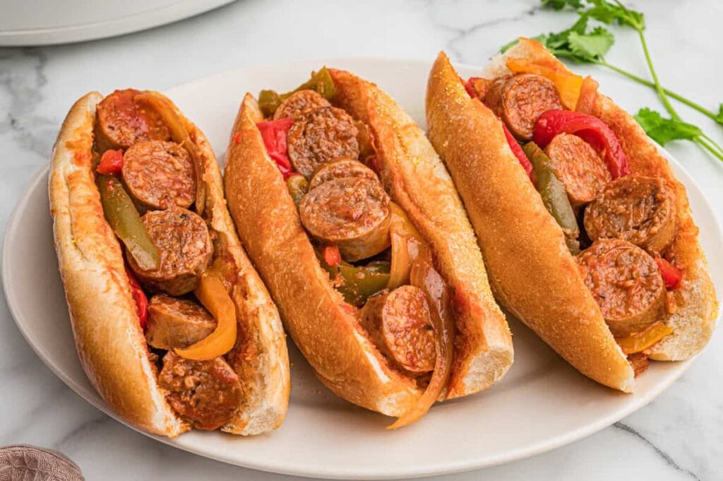 Crockpot sausage and peppers in sandwich rolls on a plate.
