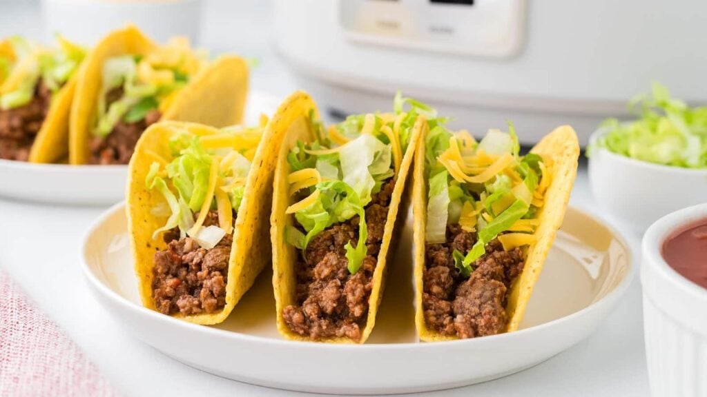 Crockpot taco meat served in crunchy tacos on a plate.