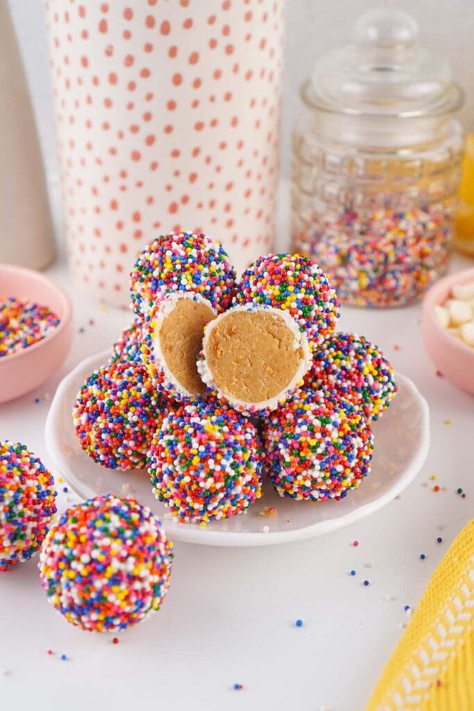 Colorful dot cake bites covered in rainbow nonpareils on a white plate.