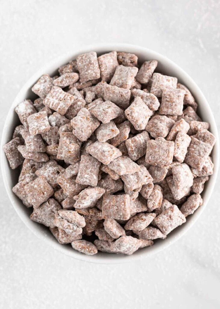 Puppy chow coated in powdered sugar in a bowl.