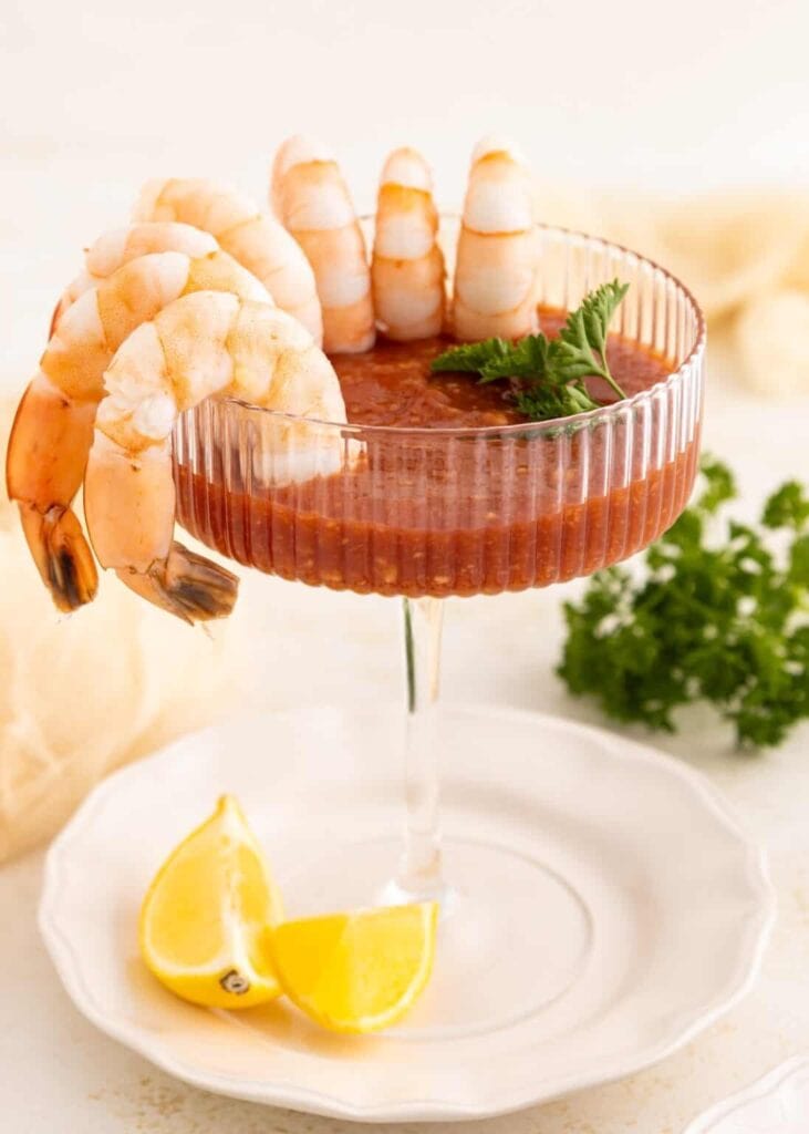 Shrimp cocktail arranged around a glass of cocktail sauce with lemon wedges.