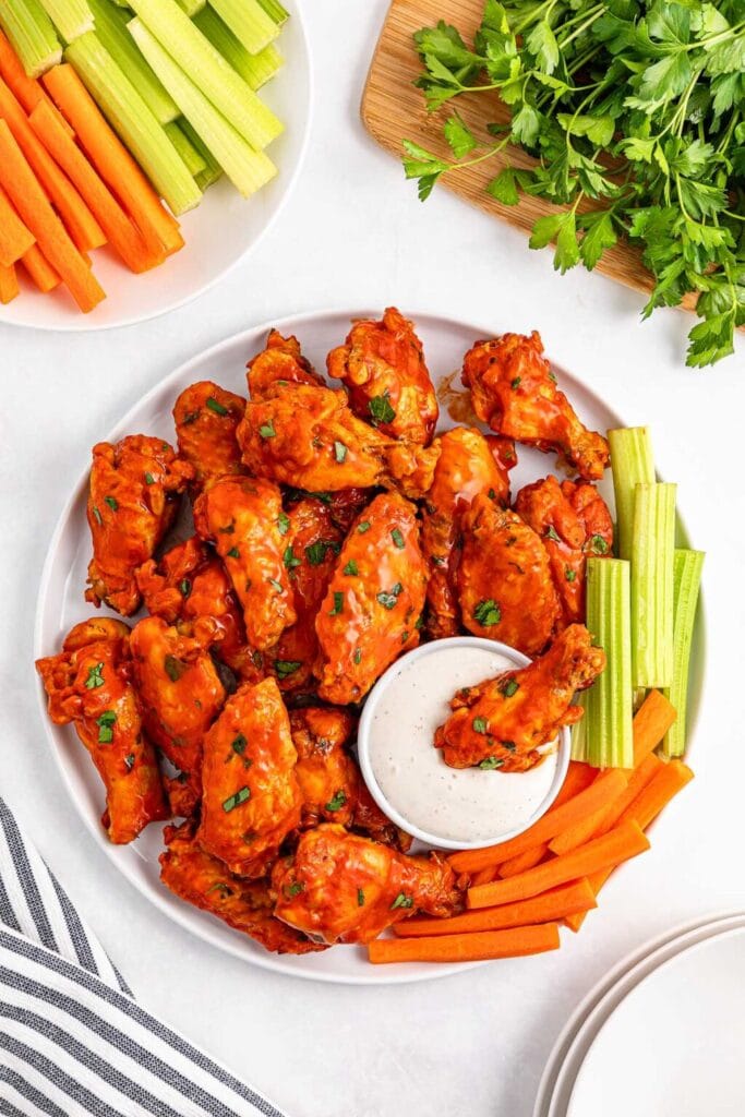 Slow cooker buffalo wings with carrots, celery, and dipping sauce on a plate.