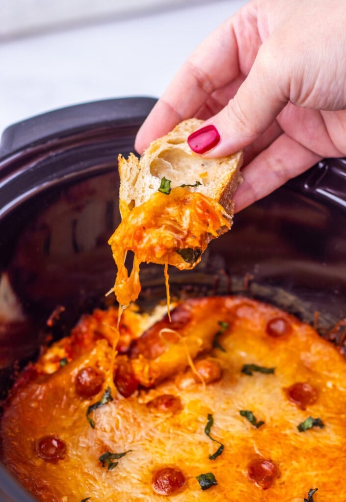 Hand dipping bread into slow cooker pizza dip.