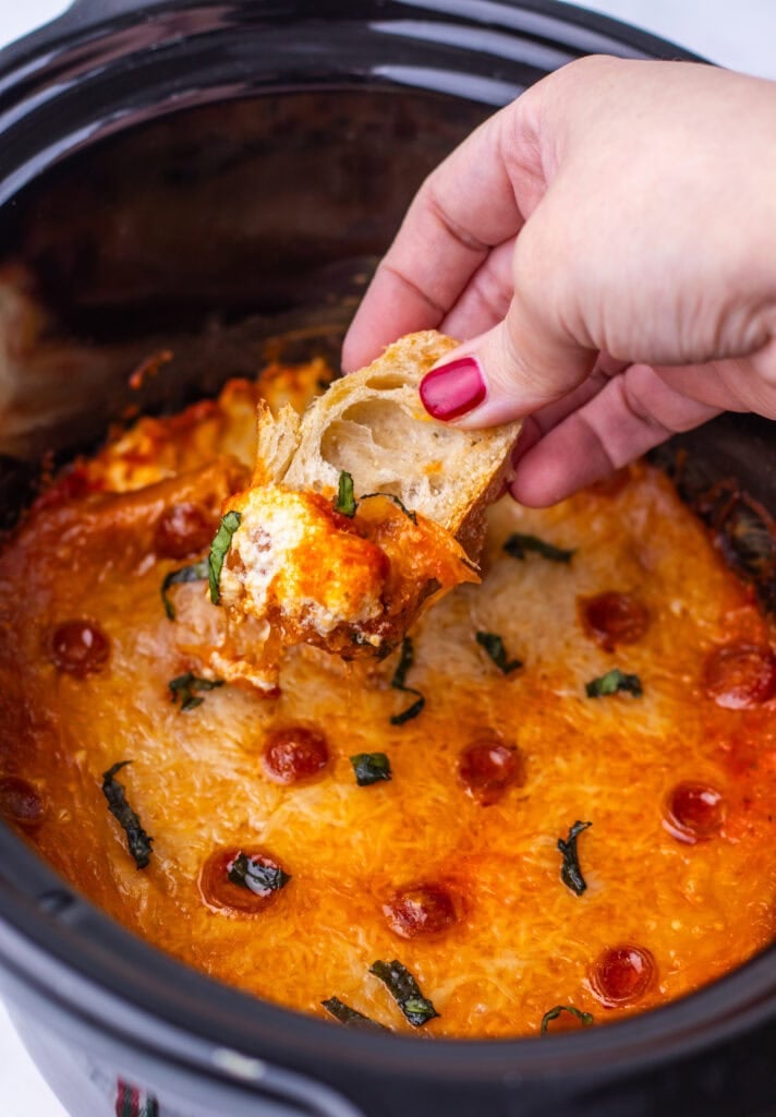 Hand dipping bread into slow cooker pizza dip.