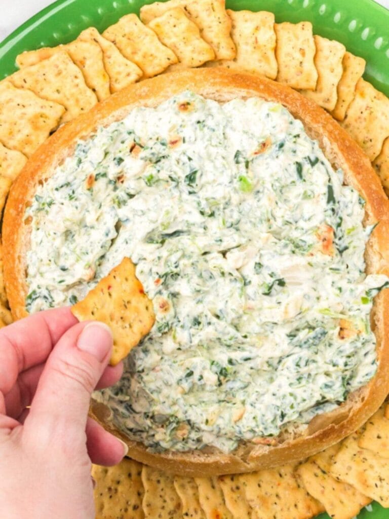 Spinach dip in a bread bowl with crackers.