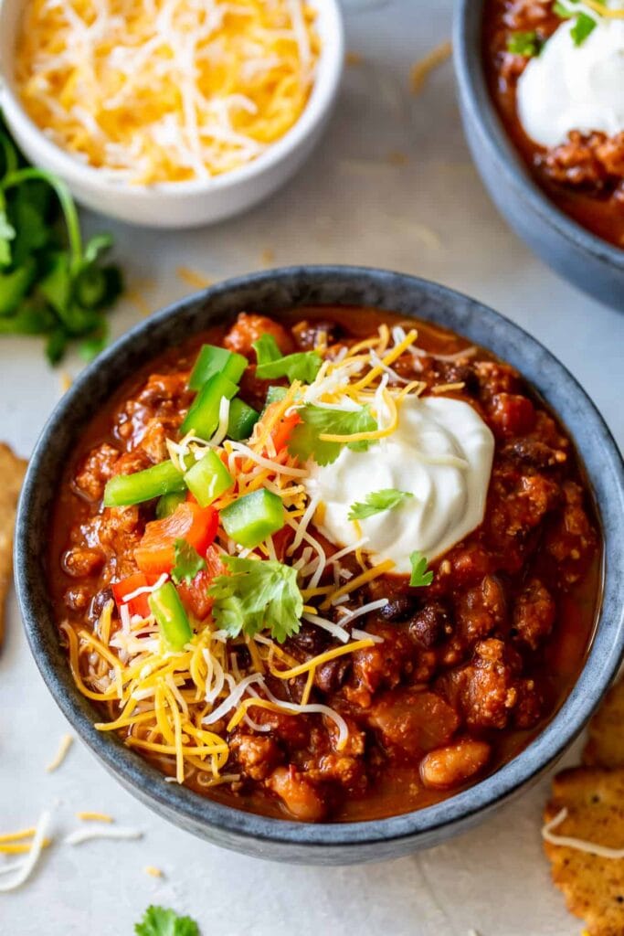 Three bean turkey chili topped with cheese and sour cream in a bowl.