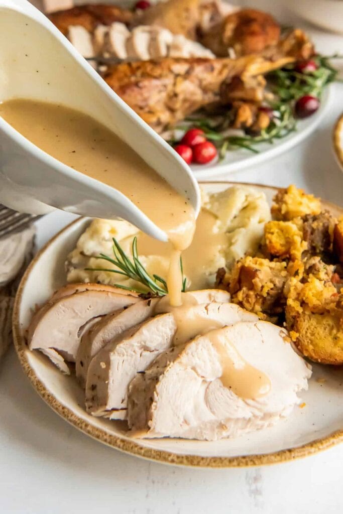 Turkey gravy being poured over sliced turkey on a plate.