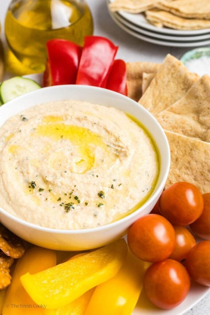 White bean dip with crackers, tomatoes, and bell peppers on the side.