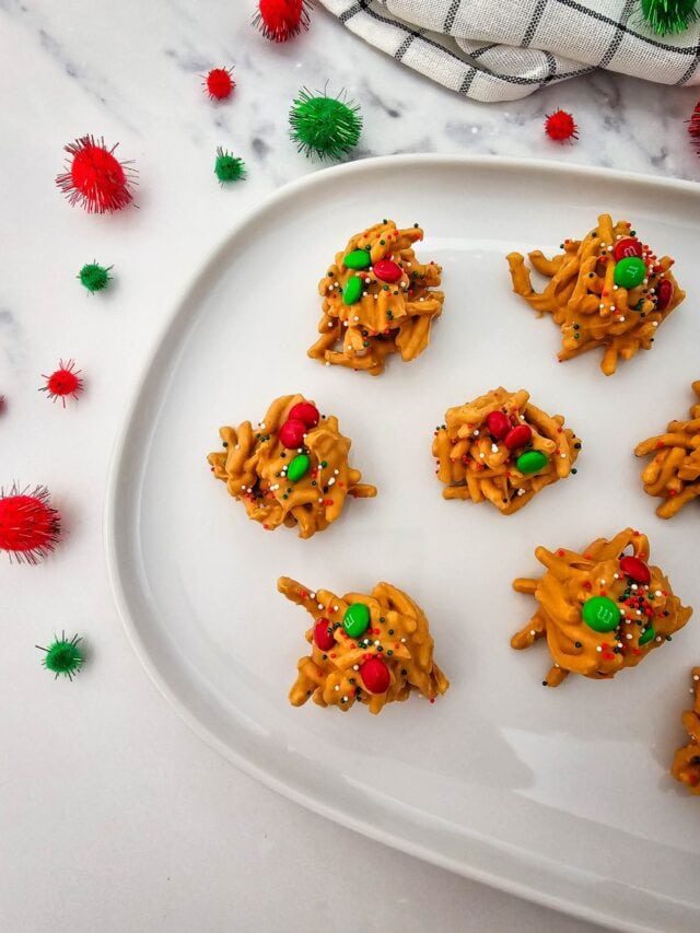 Golden chow mein clusters topped with red-green candies and sprinkles on white plate with festive pom-poms and checkered cloth.