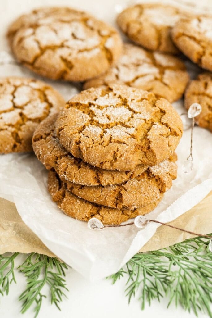 Golden cracked cookies dusted with sugar on parchment, surrounded by beads and pine foliage for holiday styling.