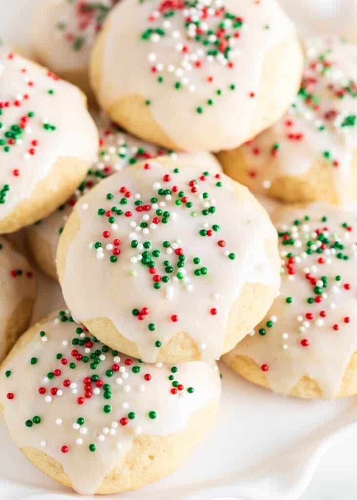 Golden cookies topped with white icing and red-green sprinkles, arranged closely on white surface.