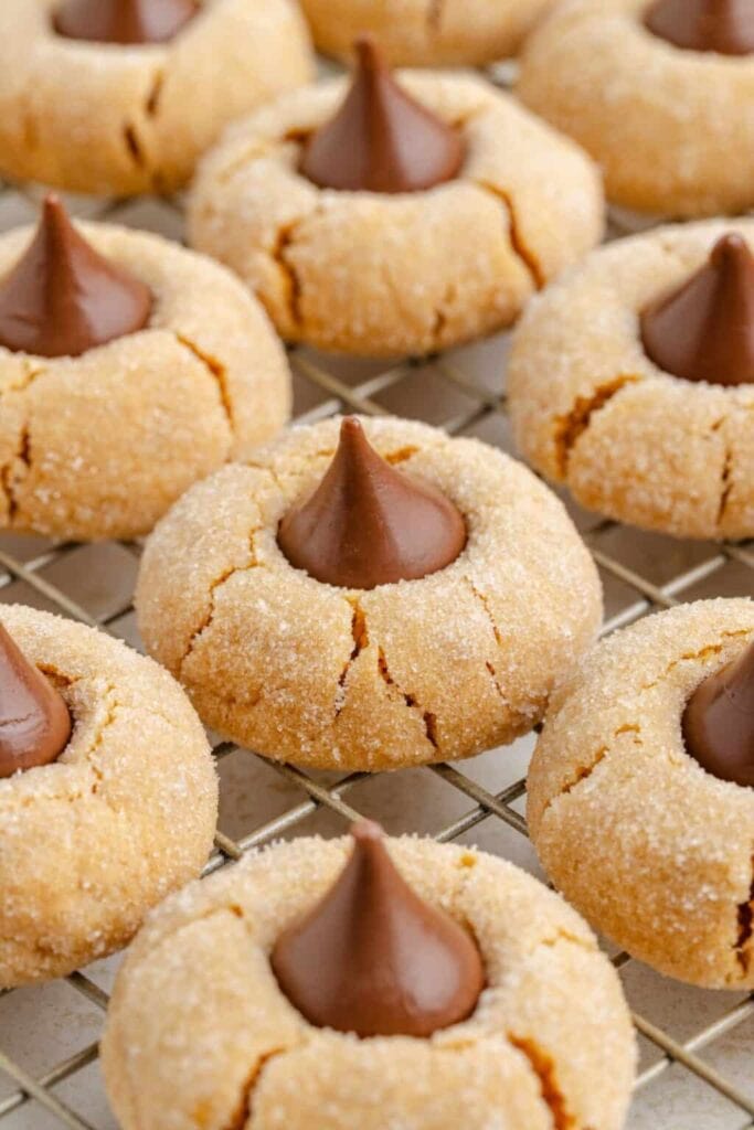 Golden peanut butter cookies with Hershey’s Kiss centers on cooling rack, lightly sugared with cracked surface.