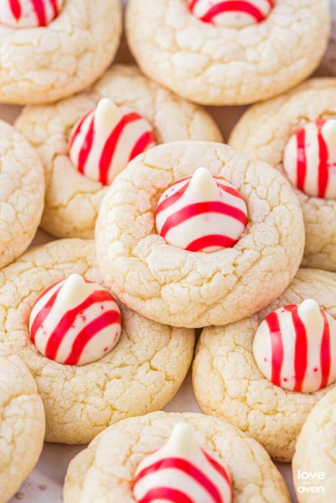 Golden cookies topped with red-white striped Hershey’s Kiss candies, arranged closely together with cracked soft texture.