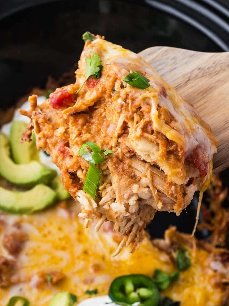 Close-up of slow cooker chicken enchilada casserole on a wooden spoon.