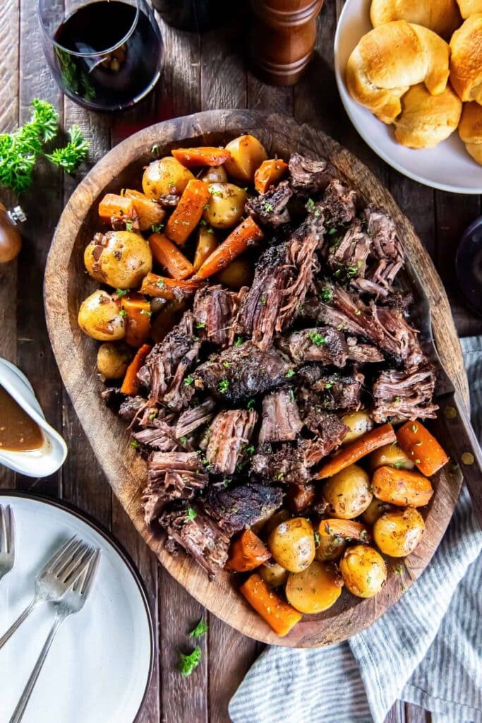 Slow cooker chuck roast with potatoes and carrots on a wooden platter.