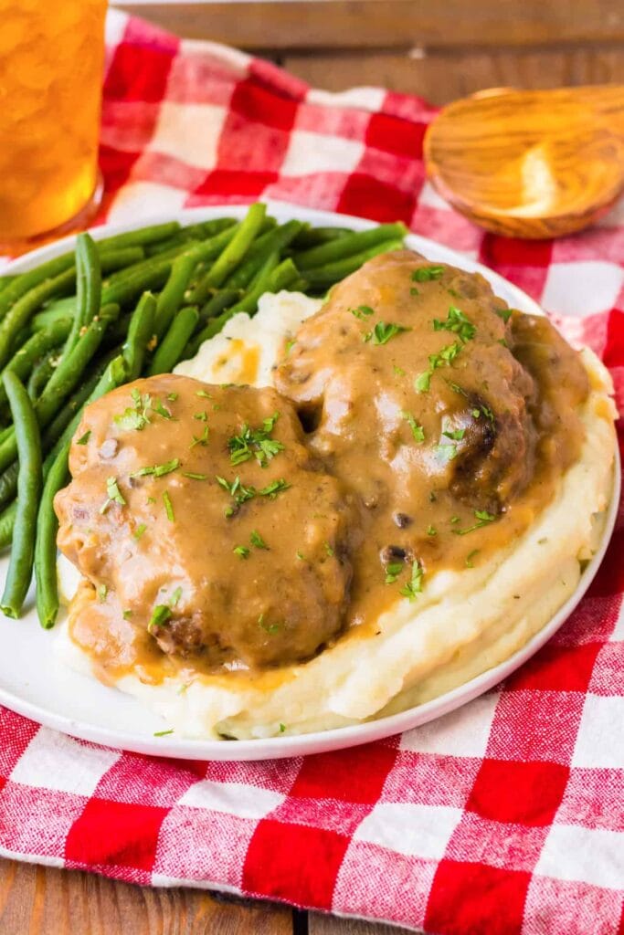 Slow cooker Salisbury steaks with mashed potatoes and green beans on a plate.