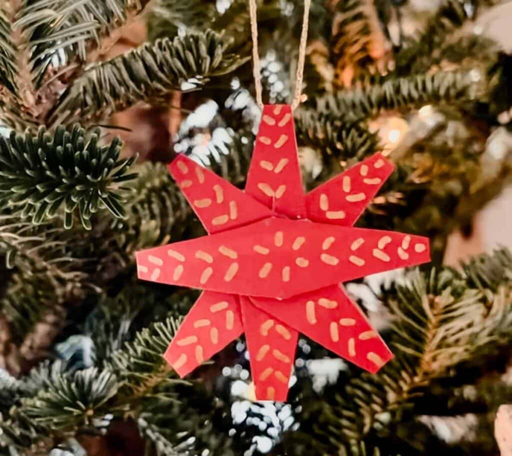 red star ornament hanging on a string on green Christmas tree branches